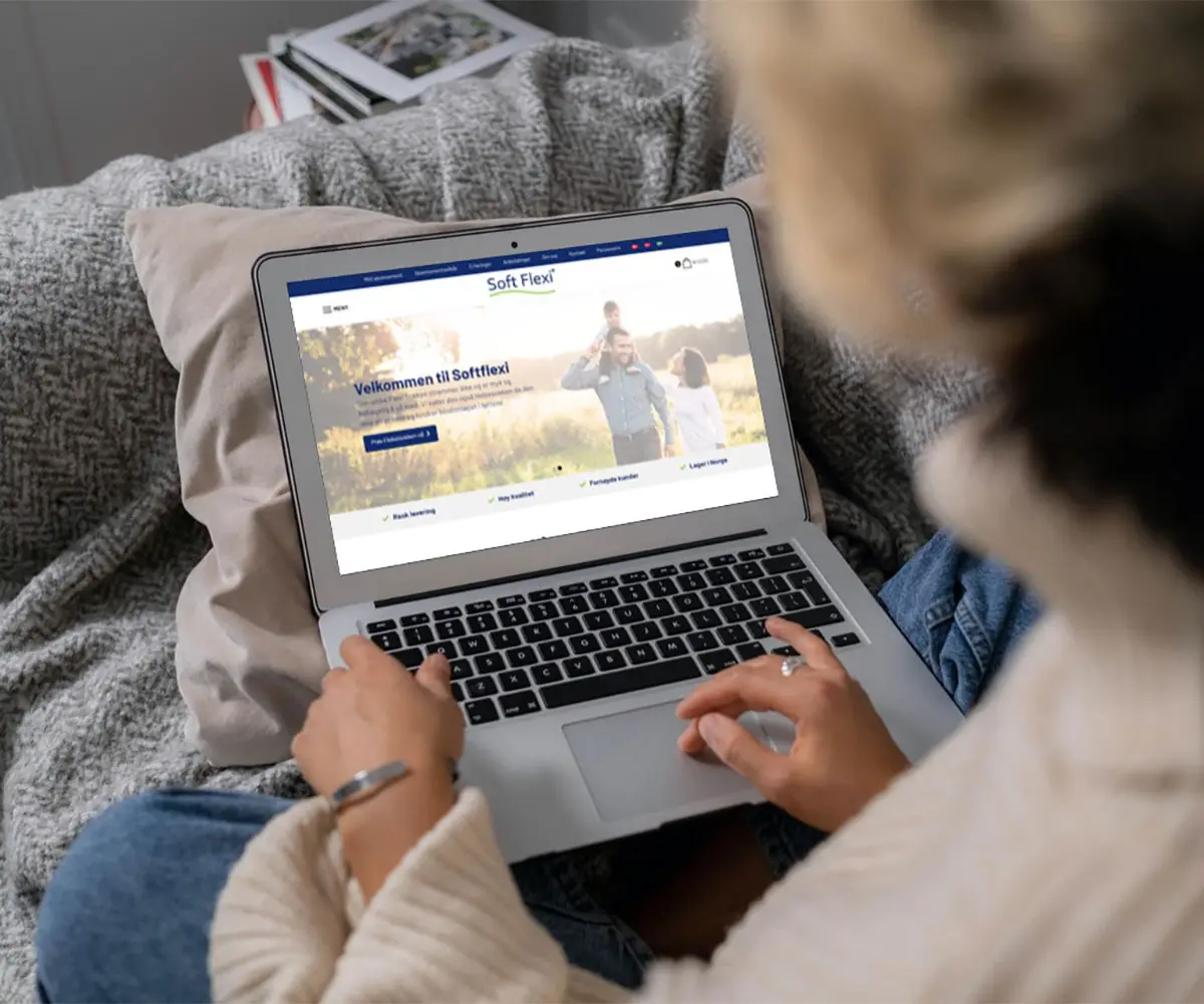 Bilde av en person som har laptop på fanget. På skjermen er det Softflexi AS sin hjemmeside, i samarbeid med UndrumDesign.