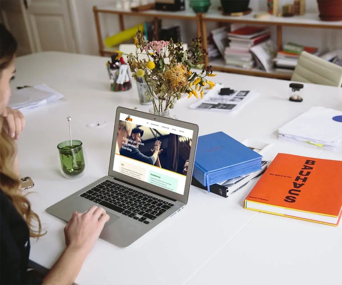 Bilde av en Person på laptopen sin på skrivebordet. På skjermen er det Guts sin hjemmeside, i samarbeid med UndrumDesign.