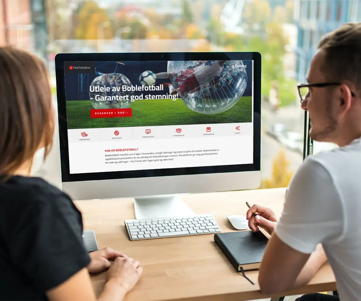 Bilde av to personer foran en Mac skjerm. På skjermen er det Festfotball AS sin hjemmeside, i samarbeid med UndrumDesign.
