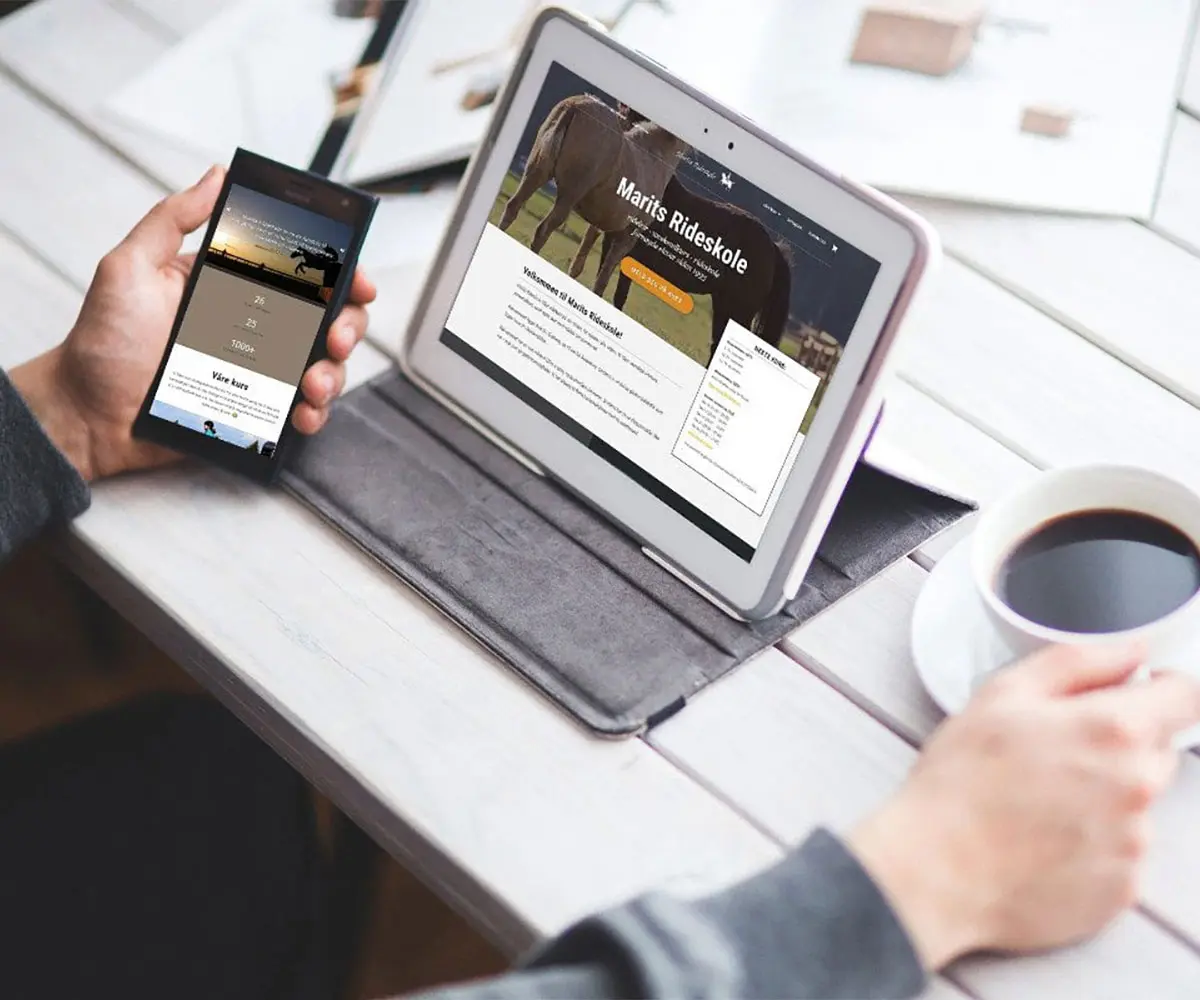Bilde av person med mobil og kaffe i hendene og tablet oppå bord. På skjermen er det Maritsrideskole sin hjemmeside i sammarbeid med UndrumDesign.