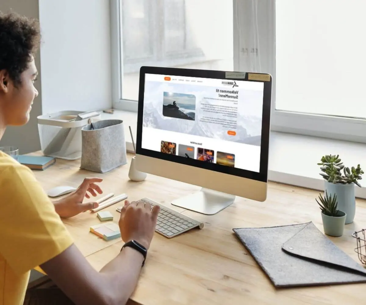 Bilde av en person som jobber på skrivebordet med en Mac skjerm. På skjermen er det SunneMenn sin hjemmeside, i samarbeid med UndrumDesign.